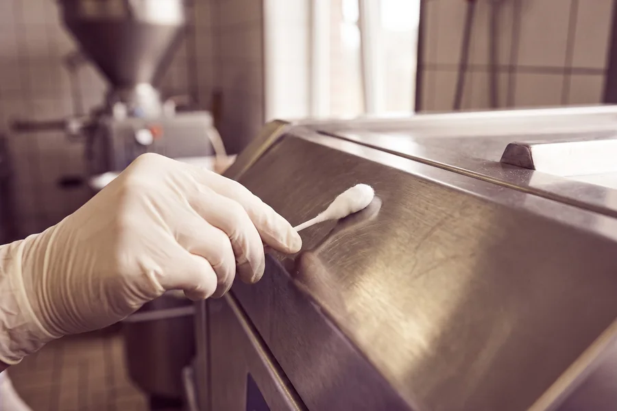 Gloved hand swabbing a stainless-steel surface for environmental monitoring